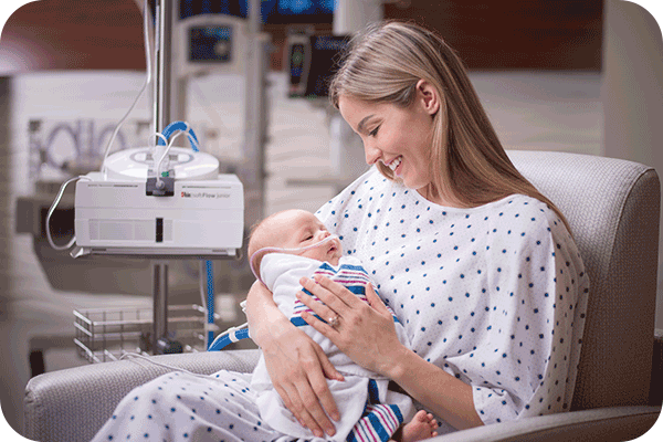mother holding baby in arms while baby is connected to Masimo softflow