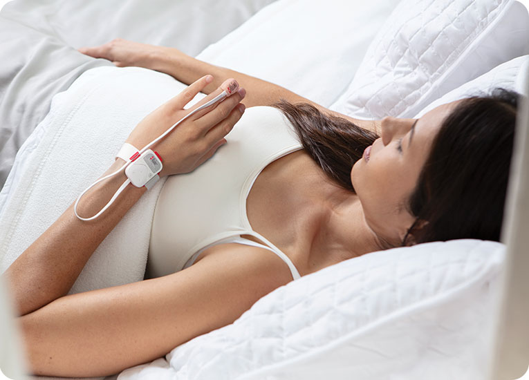 Masimo - Woman laying on bed with device on left hand